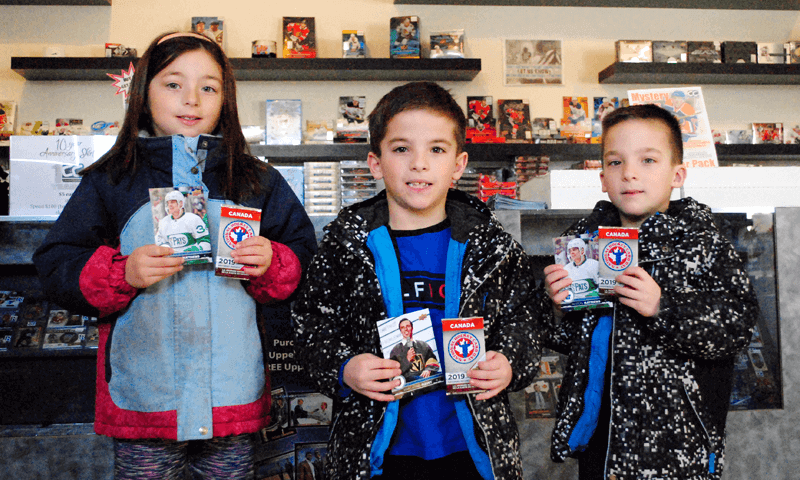 A group of 3 children holding up a pack of hockey cards for National Hockey Card Day 2019