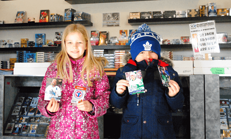 A group of 2 children holding up a pack of hockey cards for National Hockey Card Day 2019